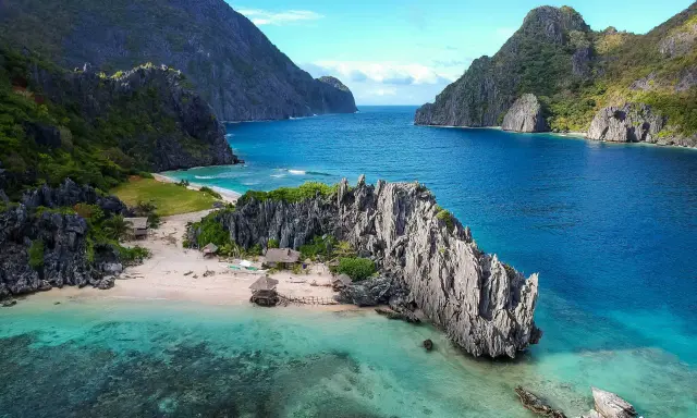 A secluded beach in the Philippines, with turquoise waters, limestone cliffs, and small huts. A perfect gay getaway in paradise.