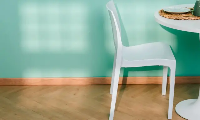 Un battiscopa in legno chiaro completa l'arredamento di una stanza con parete verde acqua, sedia bianca e tavolo.