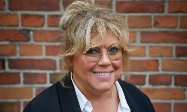 Marie Nilsson Lind ler mot kameran, med sitt blonda hår uppsatt och runda glasögon.