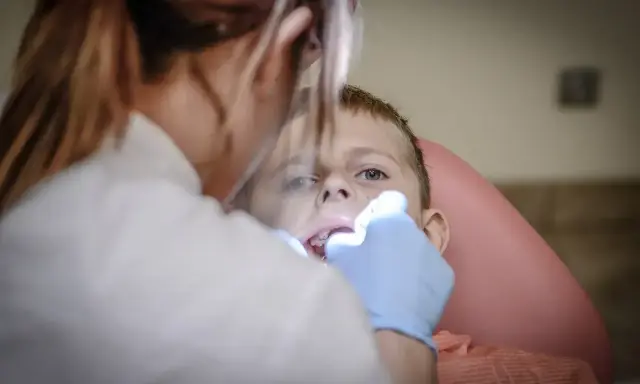 Chłopiec nie chce otworzyć ust u dentysty. Stomatolog próbuje go zbadać.