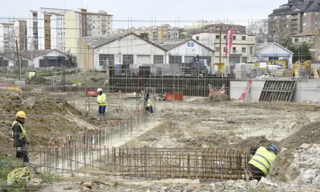 Obreros trabajan en la preparación de cimientos para nuevos proyectos de construcción. Se ven varillas de acero y maquinaria pesada en un día nublado.