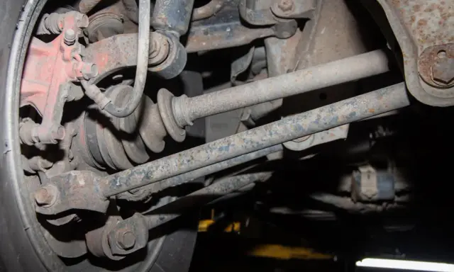 Widok od spodu na skorodowany wielowahacz z widoczną piastą, przegubem i elementami zawieszenia.