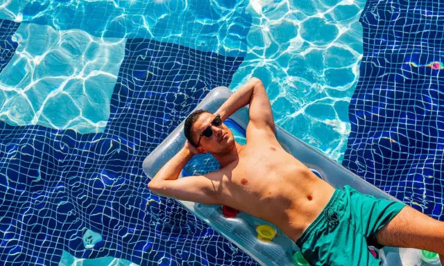 Uomo rilassato su un materassino in piscina, con gli occhiali da sole. Chissà se posso andare al mare se prendo l'antibiotico, pensa.