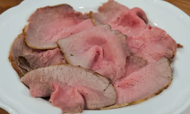 Fette sottili di arrosto di manzo rosa e succulento, servite su un piatto bianco.