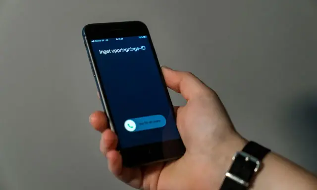 En hand håller en mobiltelefon med ett inkommande samtal. Skärmen visar "Inget uppringnings-ID" och en knapp för att svara.