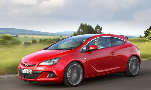 Czerwony Opel Astra J 1.4 Turbo z parą na pokładzie przemierza malowniczą trasę wśród zielonych pól i wzgórz.