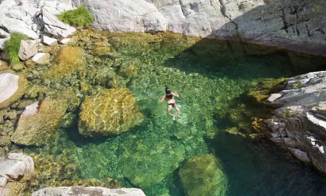 Una persona nada en unas cristalinas piscinas naturales Gredos, rodeadas de rocas y vegetación.