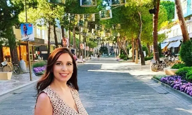 Donna sorridente in una strada alberata con negozi e fiori viola, un'atmosfera estiva nel centro di Milano Marittima.