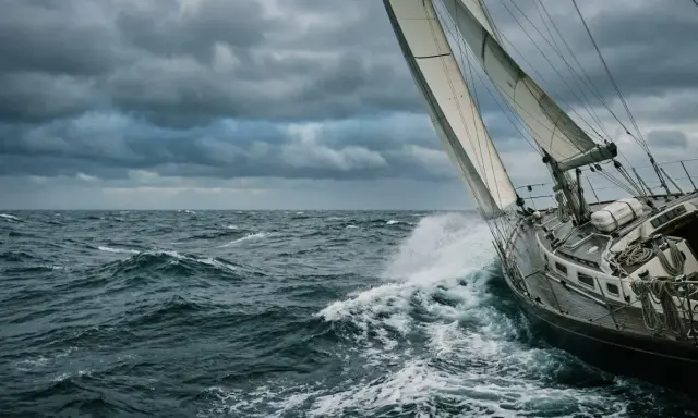 Un voilier fend les vagues sous un ciel menaçant. La proue découpe l'écume, le vent gonfle les voiles.