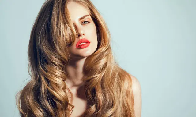 Kobieta z burzą falujących, blond włosów w stylu wolf cut, z wyrazistą czerwoną szminką.