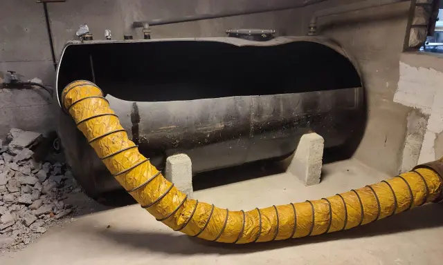 Gros réservoir de fioul noir, vide, avec un tuyau jaune flexible. Projet ma prime rénov cuve fioul en cours.