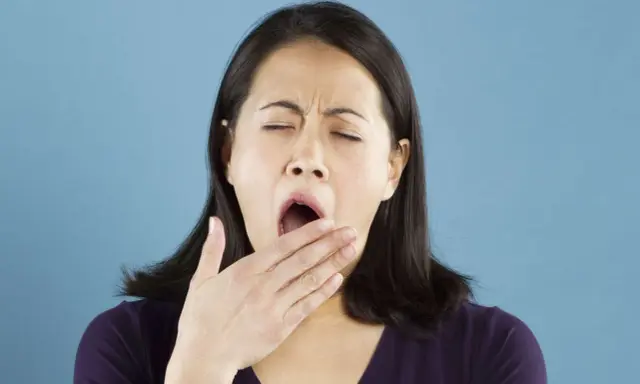 Une femme bâille, la main devant la bouche. Elle semble avoir besoin d'une pause pour réviser la conjugaison.