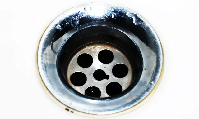 Gouttes d'eau stagnent dans un évier bouché mais pas de bouchon visible. Le métal du siphon est sale et usé.