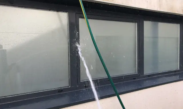 Agua salpicando sobre un perfil de aluminio de ventana, creando condensación y gotas.