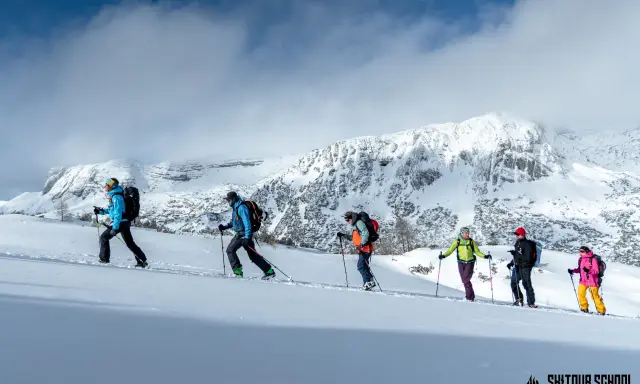 Grupa ludzi na skitouringu wspina się po ośnieżonych zboczach gór. To właśnie skitouring co to za aktywność!