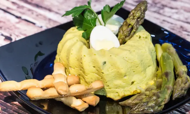 Delizioso flan di asparagi, guarnito con uovo sodo, asparagi freschi e grissini croccanti su un piatto nero.