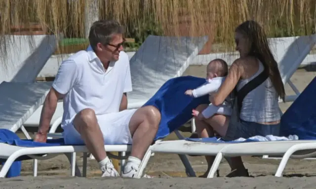 Hugh Grant njuter av stranden med sitt barn och en kvinna.
