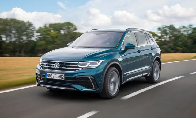 Un Volkswagen Tiguan R-Line verde oscuro se desplaza por una carretera rural, con campos dorados y árboles borrosos al fondo.