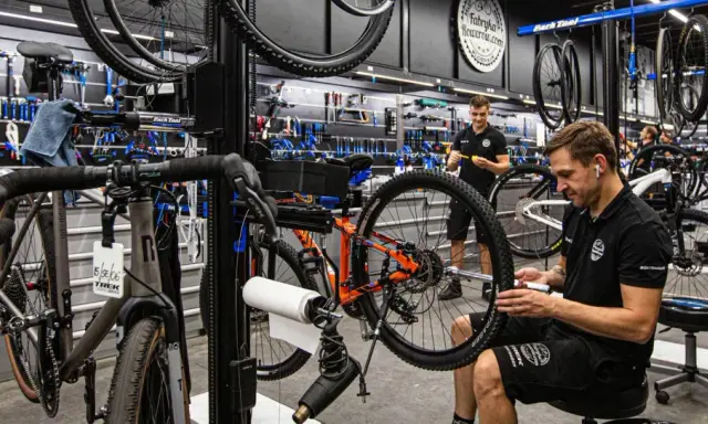 W warsztacie fabryki rowerów mechanik naprawia rower. W tle wiszą rowery i narzędzia.