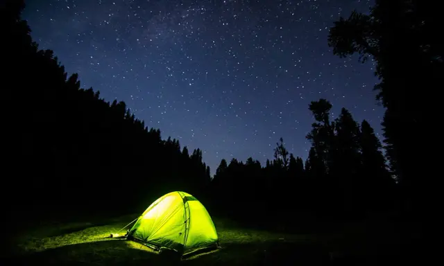 Tenda illuminata nella notte stellata, un invito a dormire in tenda immersi nella natura.