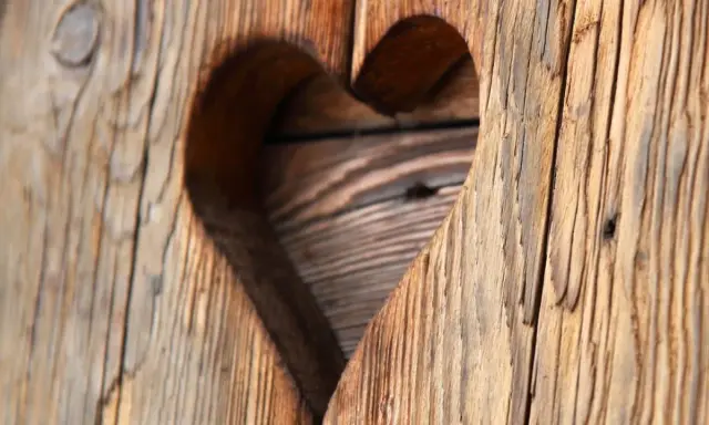 Corazón tallado en madera con textura de envejecer madera, mostrando vetas y grietas que cuentan historias.