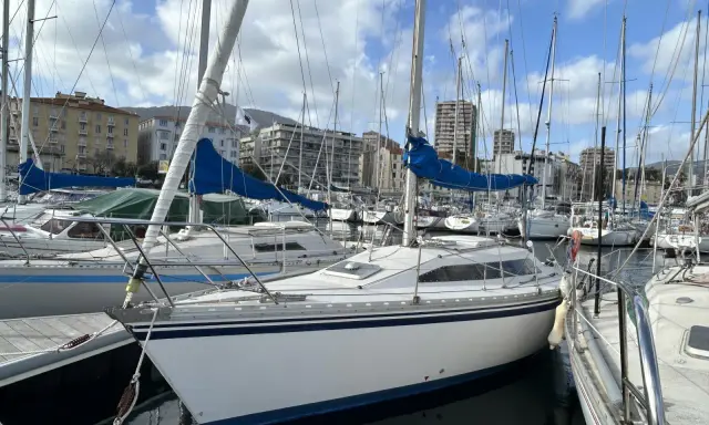 Un voilier blanc aux voiles bleues, amarré dans un port. L'avis sur ce voilier rush est qu'il est prêt pour la prochaine aventure.
