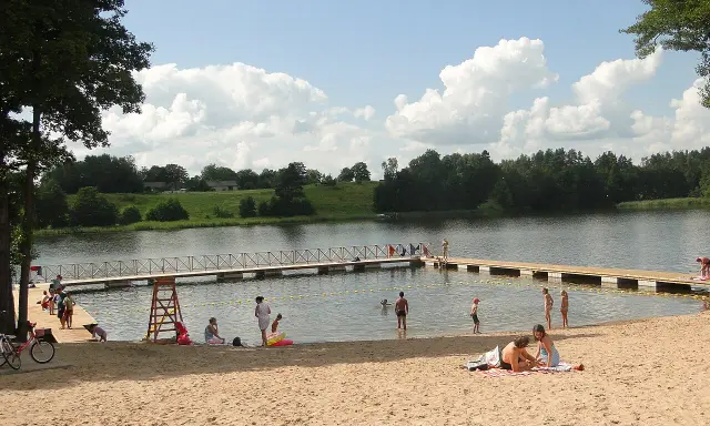 Słoneczny dzień na jednej z najpiękniejszych plaż na Mazurach. Ludzie odpoczywają na piaszczystym brzegu i w wodzie, ciesząc się latem.