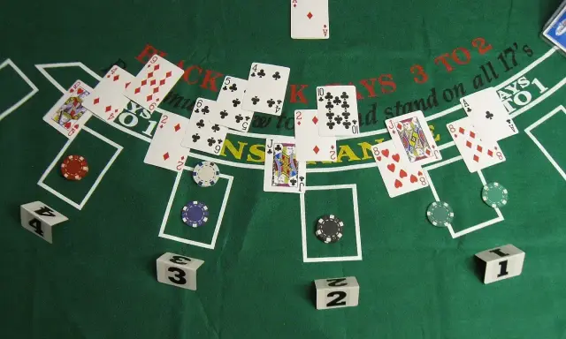 Stół do gry w blackjacka, karty i żetony. Widać karty z numerami i figurami, a także napisy "BLACKJACKS 3 TO 2" i "stand on all 17's".