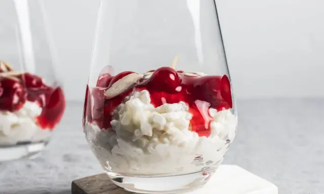 Delicioso arroz con leche asturiano cremoso, coronado con cerezas rojas y almendras laminadas en un vaso.