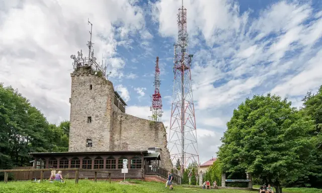 Kamienna wieża widokowa na Chełmcu, obok niej wysokie maszty telekomunikacyjne. Ludzie odpoczywają na trawie.