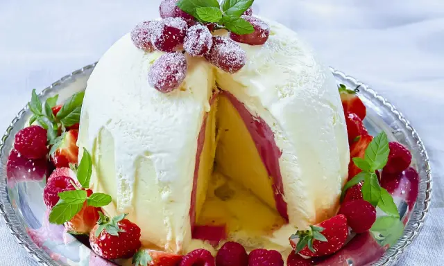 En imponerande dessert till nyår: en kupolformad glassbakelse med lager av gul och rosa glass, dekorerad med färska bär och mynta.