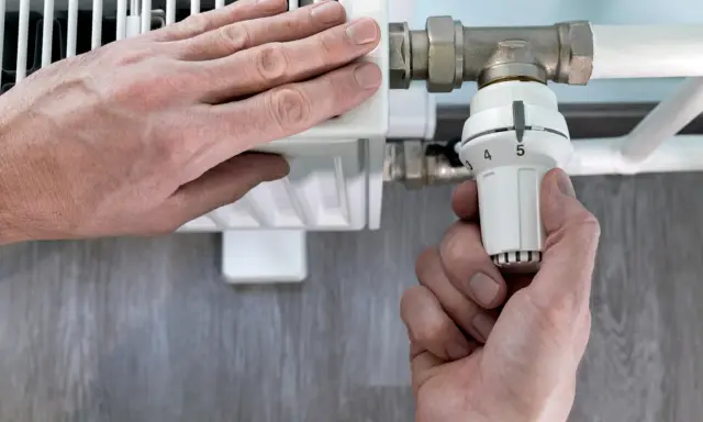 Mano ajusta el termostato de un radiador. El radiador solo calienta la mitad derecha, indicando un posible problema.