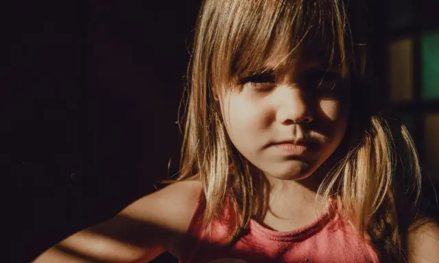 Niña con expresión seria, con luz de ventana en su rostro. A veces, mi hijo de 9 años se enoja por todo, pero hoy solo mira con intensidad.