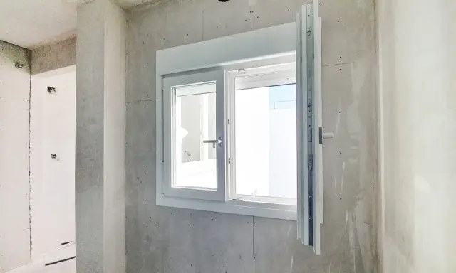Instalar ventana PVC en obra gris. Ventana blanca de doble cristal con manilla plateada, lista para ser fijada.