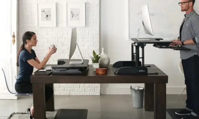 Un homme et une femme travaillent sur des bureaux réglables en hauteur. Une pause obligatoire pour le travail debout est essentielle pour leur bien-être.