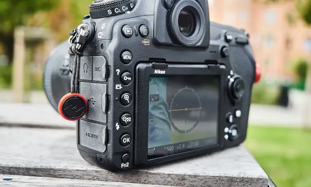 Nikon D850 test w plenerze. Aparat leży na drewnianym stole, w tle zieleń i budynek.