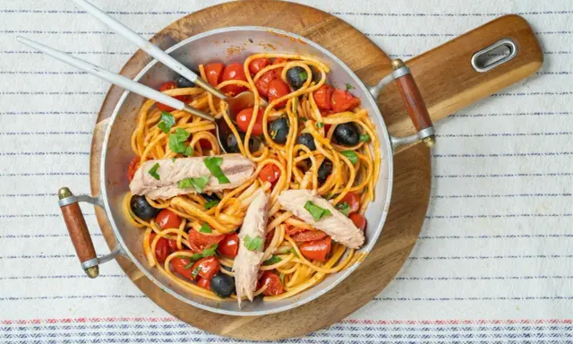 Pyszne spaghetti alla puttanesca z tuńczykiem, pomidorkami i czarnymi oliwkami w metalowej patelni, gotowe do podania.
