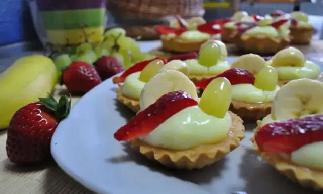 Pyszne babeczki z budyniem, udekorowane truskawkami, bananami i winogronami, wyglądają apetycznie.