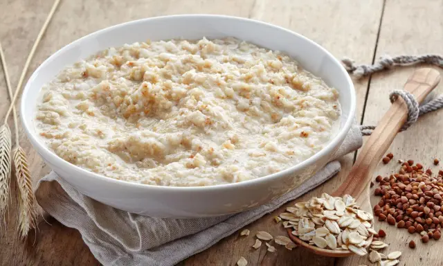 Schüssel mit Haferbrei, daneben Haferflocken und Buchweizen. Gute Haferkur Erfahrungen beginnen mit einem gesunden Frühstück.