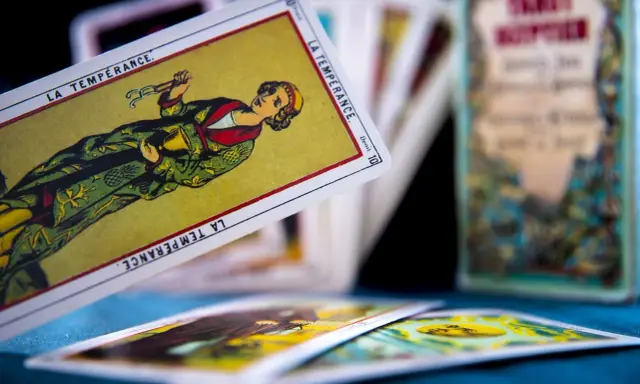 Rozłożone karty tarot 3 karty: "La Tempérance" w centrum, inne karty w tle i pudełko z napisem "Tarot".