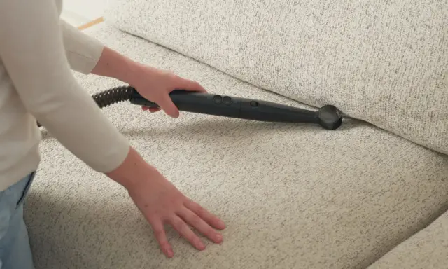 Person rengör soffa med ångtvätt för att få bort dålig lukt från ny matta.