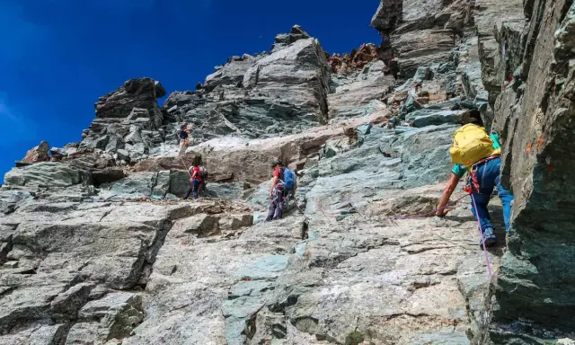 Alpinisti scalano la roccia sul Monviso, seguendo la via normale. Un'avventura sotto il cielo azzurro.