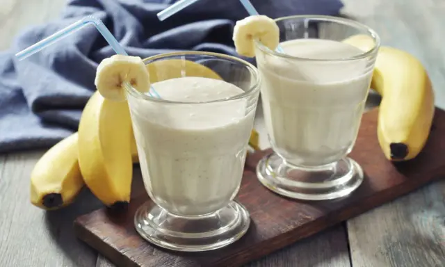 Dwa bananowe koktajle proteinowe w szklankach z rurkami i plasterkami banana. Idealne, gdy pić shake proteinowy po treningu.