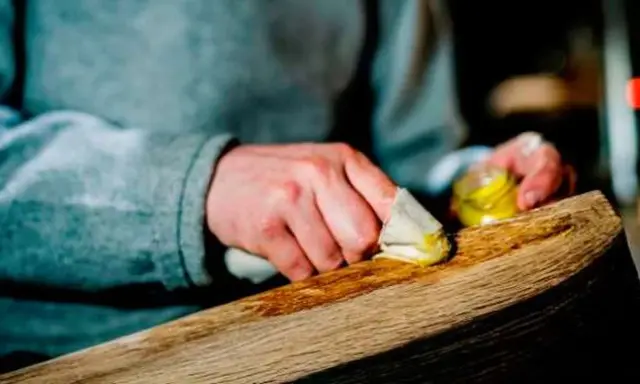 Manos aplicando cera a un trozo de madera, restaurando su brillo. El proceso de decapar madera revela su belleza natural.