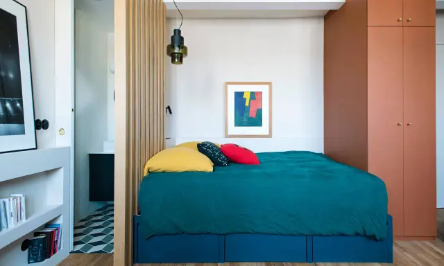 Une chambre cabine cosy avec un lit bleu canard, des coussins colorés et une armoire ocre. Un paravent en bois sépare l'espace nuit de la salle de bain.