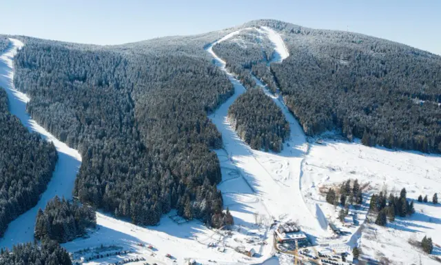Widok z lotu ptaka na czarna góra resort, ośrodek górski z trasami narciarskimi wśród ośnieżonych lasów i budynkami u podnóża góry.