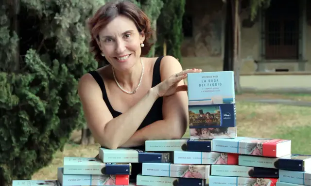 Stefania Auci sorride, circondata dai suoi libri "I Leoni di Sicilia" e "L'inverno dei leoni", celebrando il successo della saga.