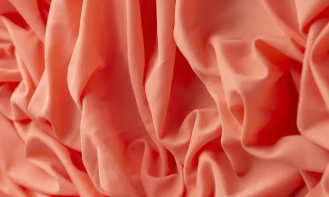 Tessuto arancione con pieghe morbide. Il materiale acrilico, cos'è? Una fibra sintetica versatile e resistente, ideale per abbigliamento e tessuti d'arredo.
