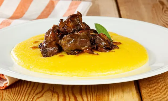 Piatto di polenta e osei, con uccellini scuri in umido e una foglia di salvia.