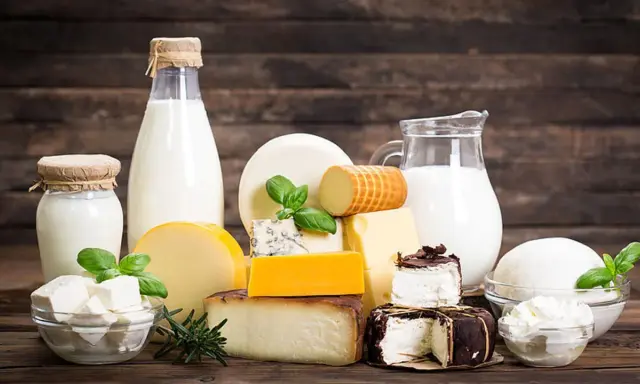 Milchprodukte wie Käse und Milch, die Laktose enthalten, sind auf einem Holztisch arrangiert.